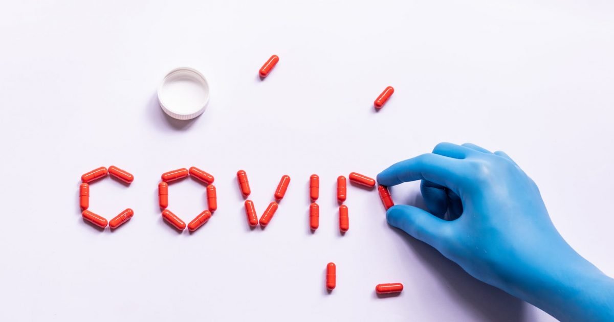 doctor in glove arranging capsules in word covid